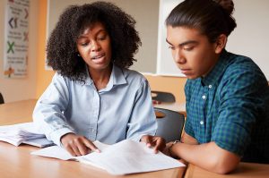 high-school-tutor-giving-male-student-one-to-one-tuition-at-desk