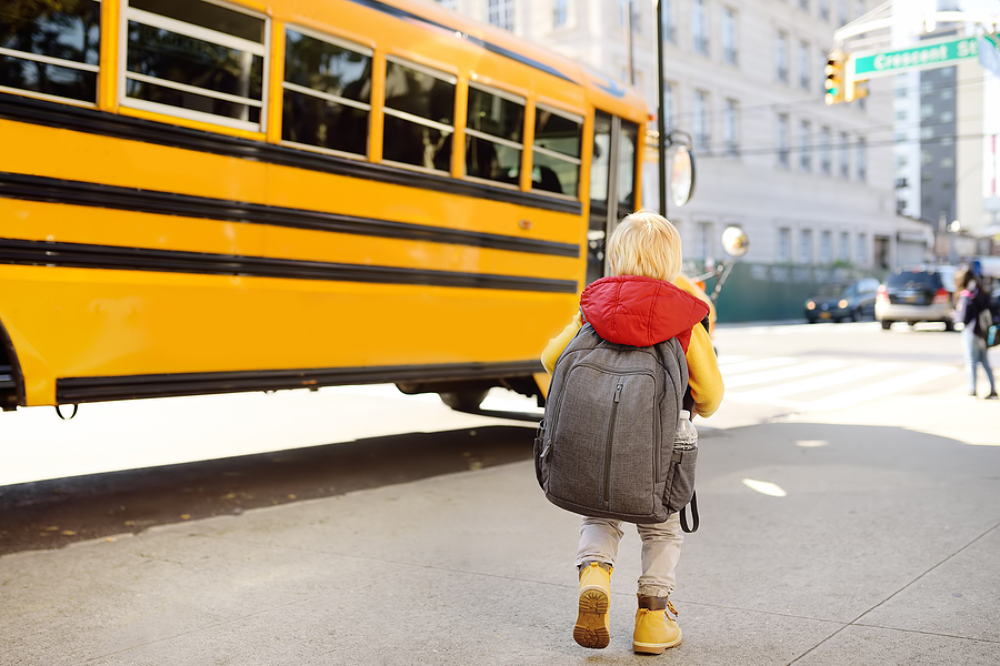 pupil-with-schoolbag-with-yellow-school-bus-on-background-back