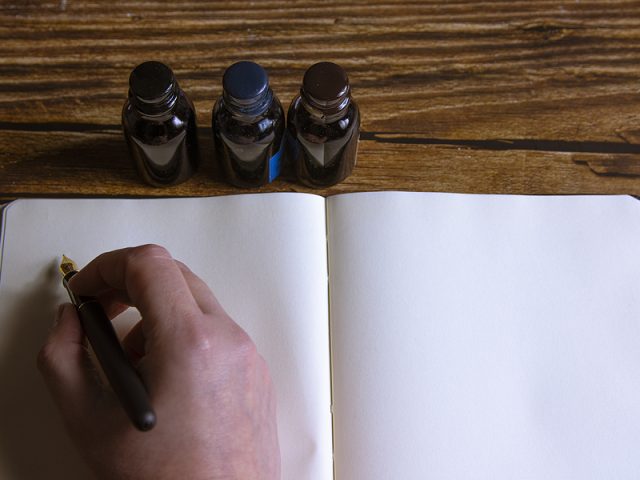 close-up-of-a-fountain-pen-on-a-notebook-and-several-inkwells-c