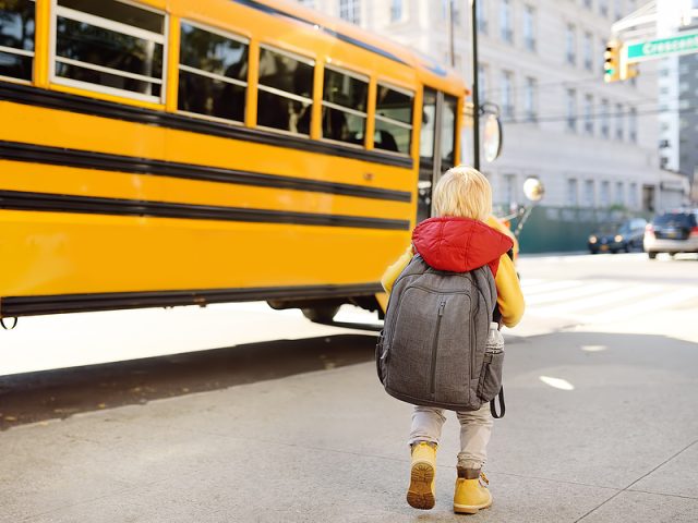 pupil-with-schoolbag-with-yellow-school-bus-on-background-back