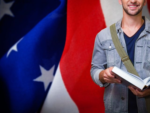 student-smiling-at-camera-in-library-against-crumbled-american-f